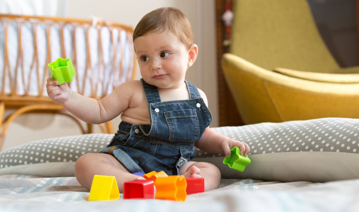 8 Monate altes Baby sitzt und spielt.