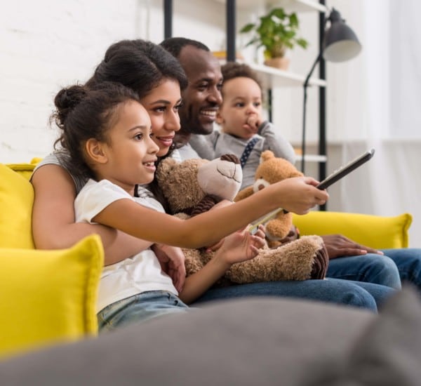 Medienkonsum: Eine vierköpfige Familie sitzt gemeinsam glücklich auf der Couch und schaut TV.