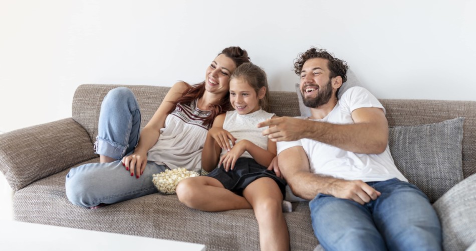 Eine Familie sitzt auf der Couch und schaut Kinderserien an.