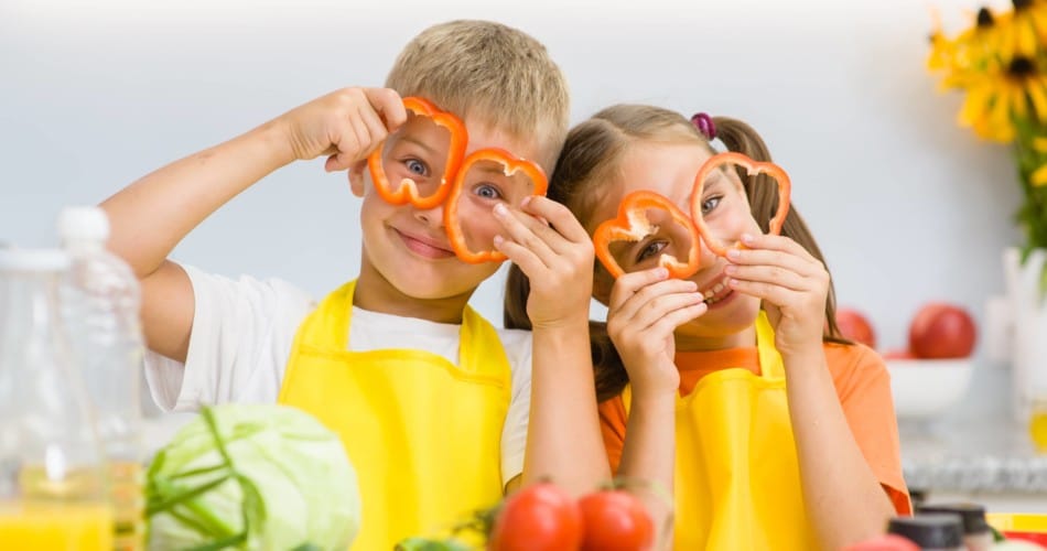 Zwei Kinder halten Paprikastücke vor ihre Augen.
