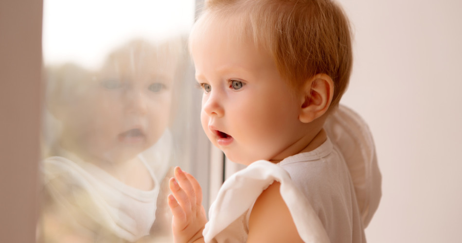 11 Monate altes Baby steht am Fenster