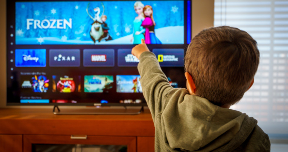 Ein Kind zeigt mit dem Finger auf den Fernseher, wo Disney Plus läuft.