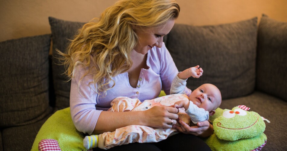 Eine Mutter, die ihr Baby auf dem Schoß hat und ein Stillkissen um sich.