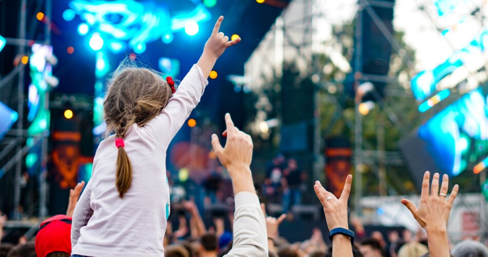 Ein kleines Mädchen auf den Schultern von Mama bzw. Papa vibet auf dem Festivalgelände zur Musik.