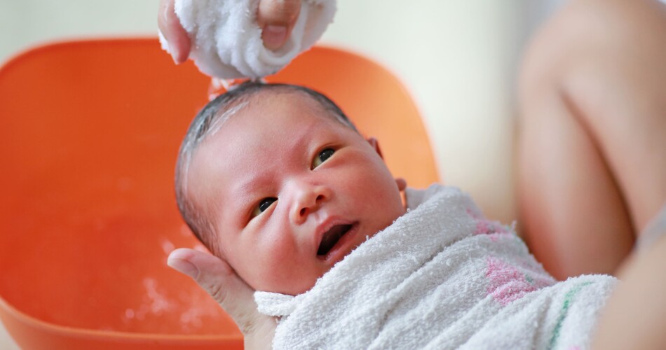 Eine Mutter wäscht die Haare ihres Babys mit einem feuchten Tuch und Shampoo