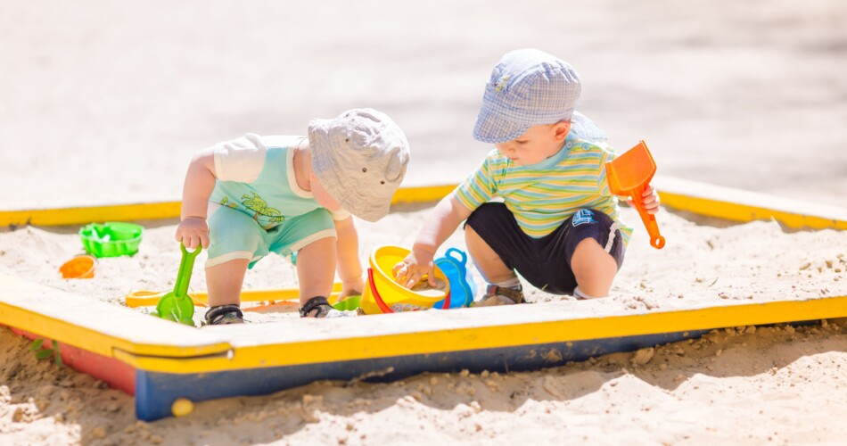 Zwei Kinder spielen mit Sandspielzeug im Sandkasten.