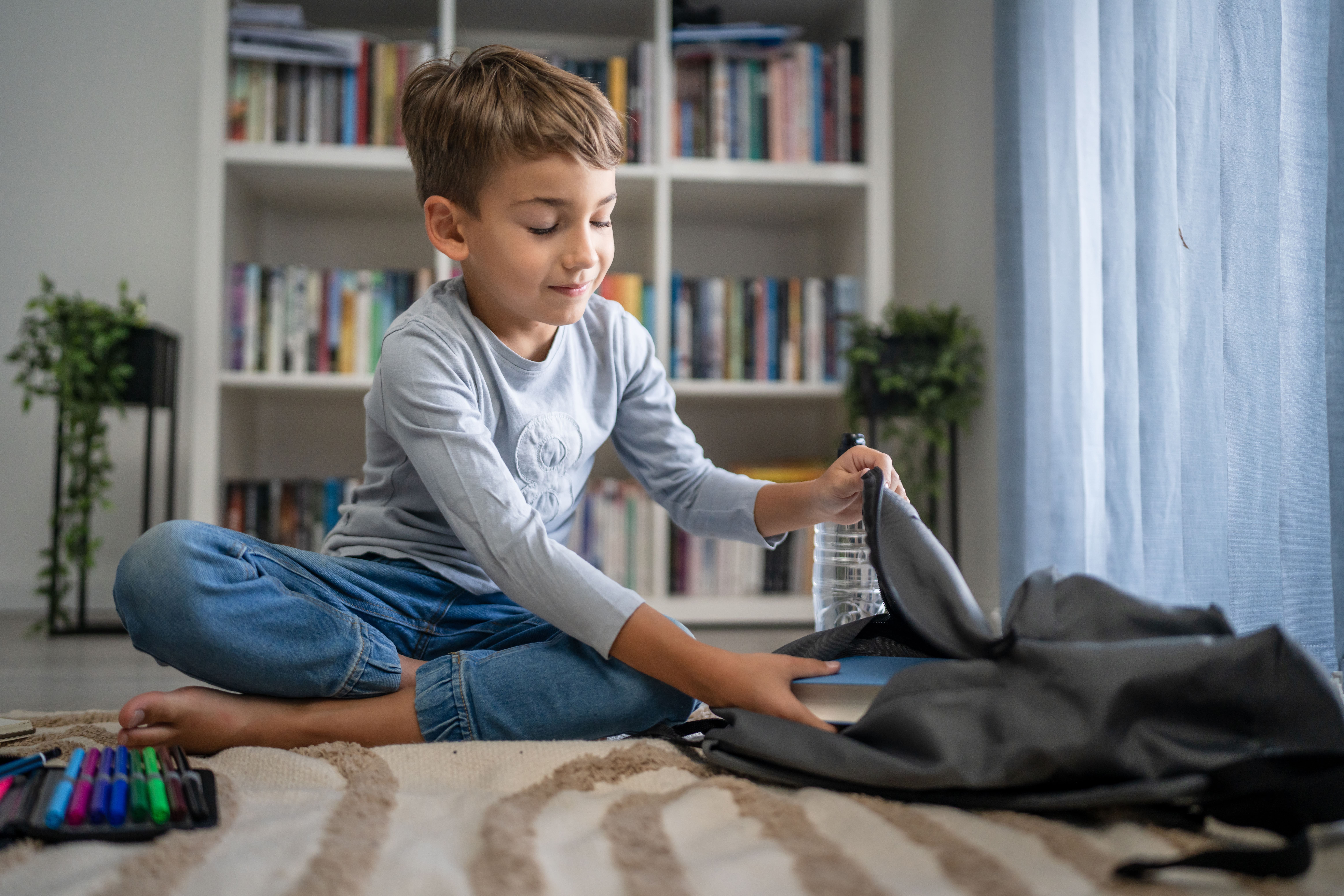 Ein Junge sitzt auf dem Boden in seinem Zimmer und packt seinen Schulranzen.