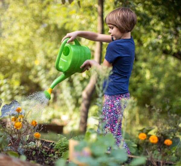 Kind gießt Pflanzen mit Gießkanne beim Gärtnern mit Kindern im April