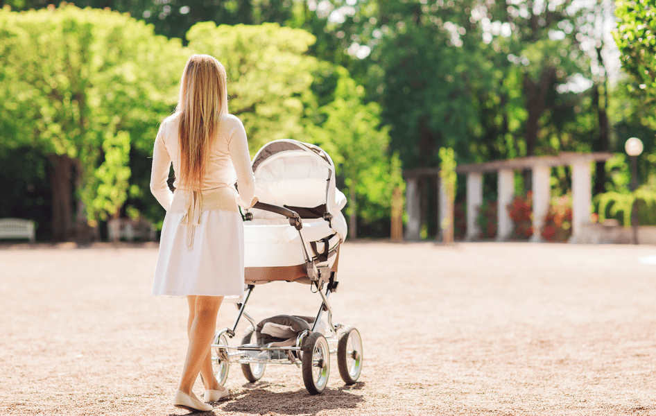 Ein Mutter schiebt ihr Baby im Kinderwagen durch den Park im Sommer
