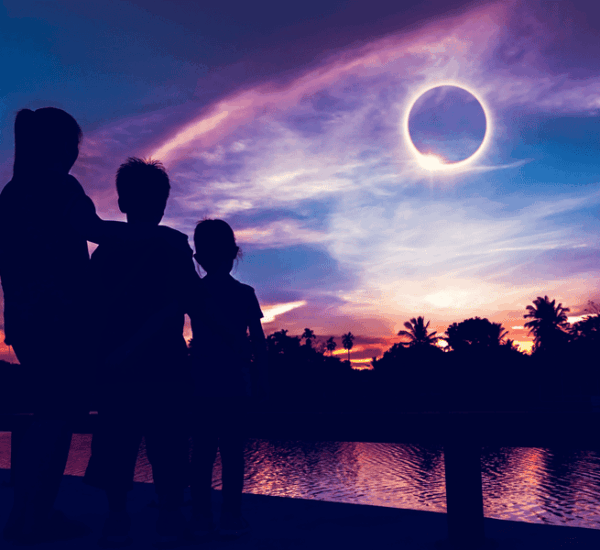 Ein Erwachsene und zwei Kinder beobachten gemeinsam eine totale Sonnenfinsternis am Himmel.