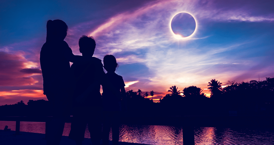 Ein Erwachsene und zwei Kinder beobachten gemeinsam eine totale Sonnenfinsternis am Himmel.