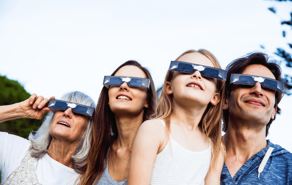 Familie beobachtet eine Sonnenfinsternis mithilfe spezieller Schutzbrillen.