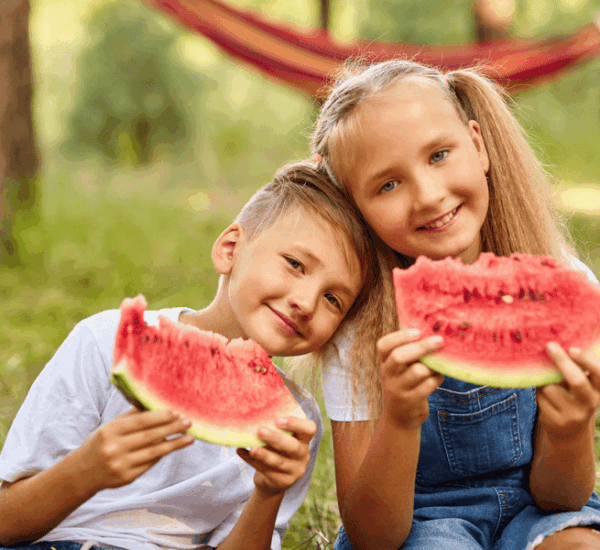 Zwei fröhliche Kinder genießen an einem Sommertag im Park saftige Stücke Wassermelone.