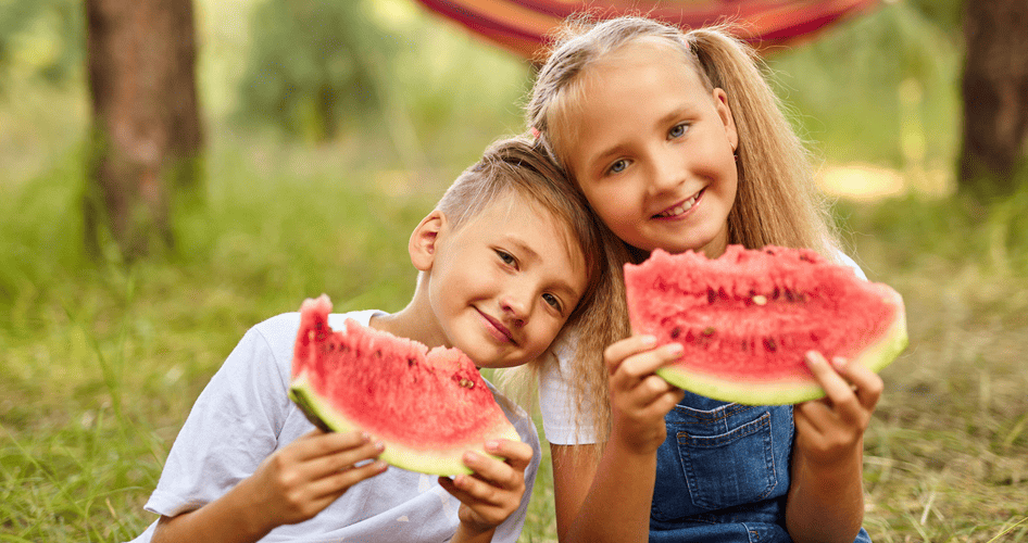 Zwei fröhliche Kinder genießen an einem Sommertag im Park saftige Stücke Wassermelone.