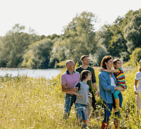 Mehrgenerationsfamilie bei einem sonnigen Spaziergang in der Natur, die Mutter hält ihre Tochter im Arm.