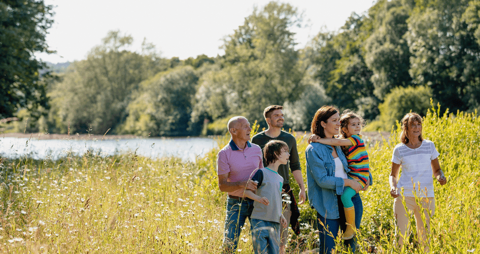 Mehrgenerationsfamilie bei einem sonnigen Spaziergang in der Natur, die Mutter hält ihre Tochter im Arm.