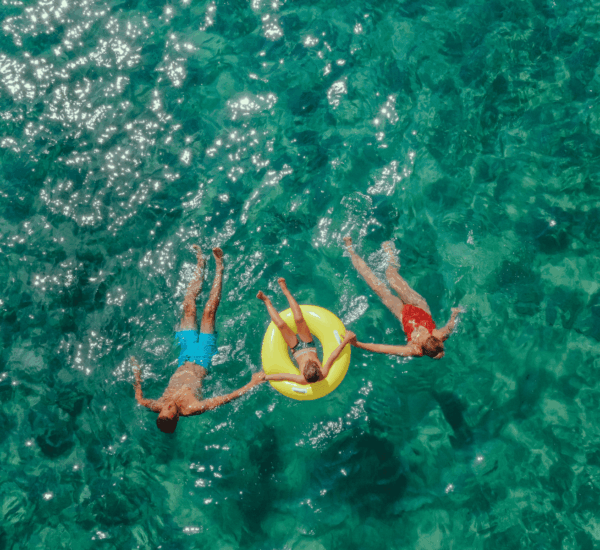 amilie schwimmt gemeinsam auf dem Rücken im Meer, die Tochter in der Mitte treibt auf einem bunten Schwimmreifen.