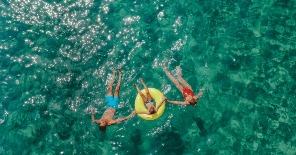 amilie schwimmt gemeinsam auf dem Rücken im Meer, die Tochter in der Mitte treibt auf einem bunten Schwimmreifen.